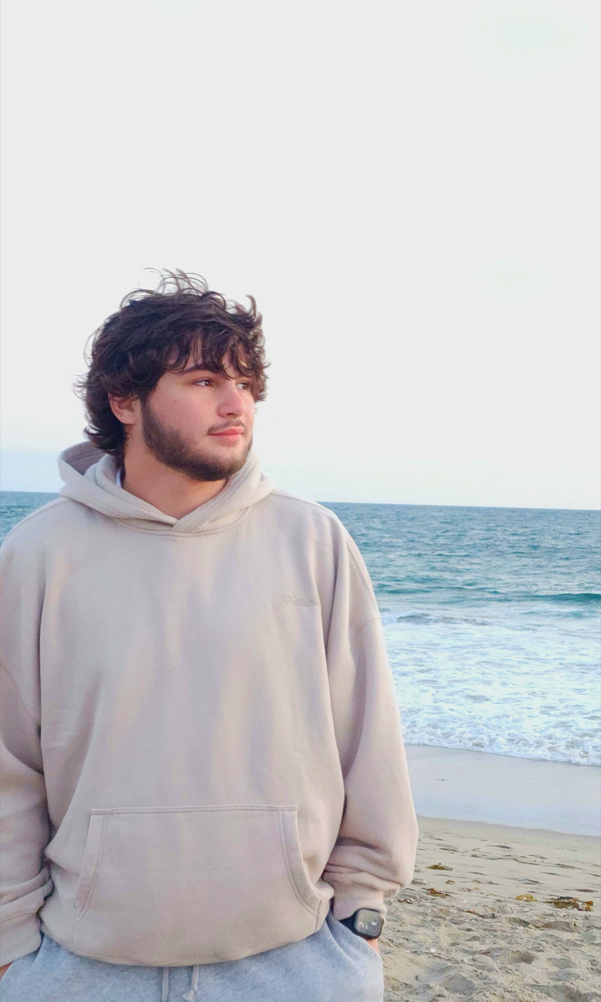 Liam Reilly on a beach, looking off to the side, in a grey hoodie